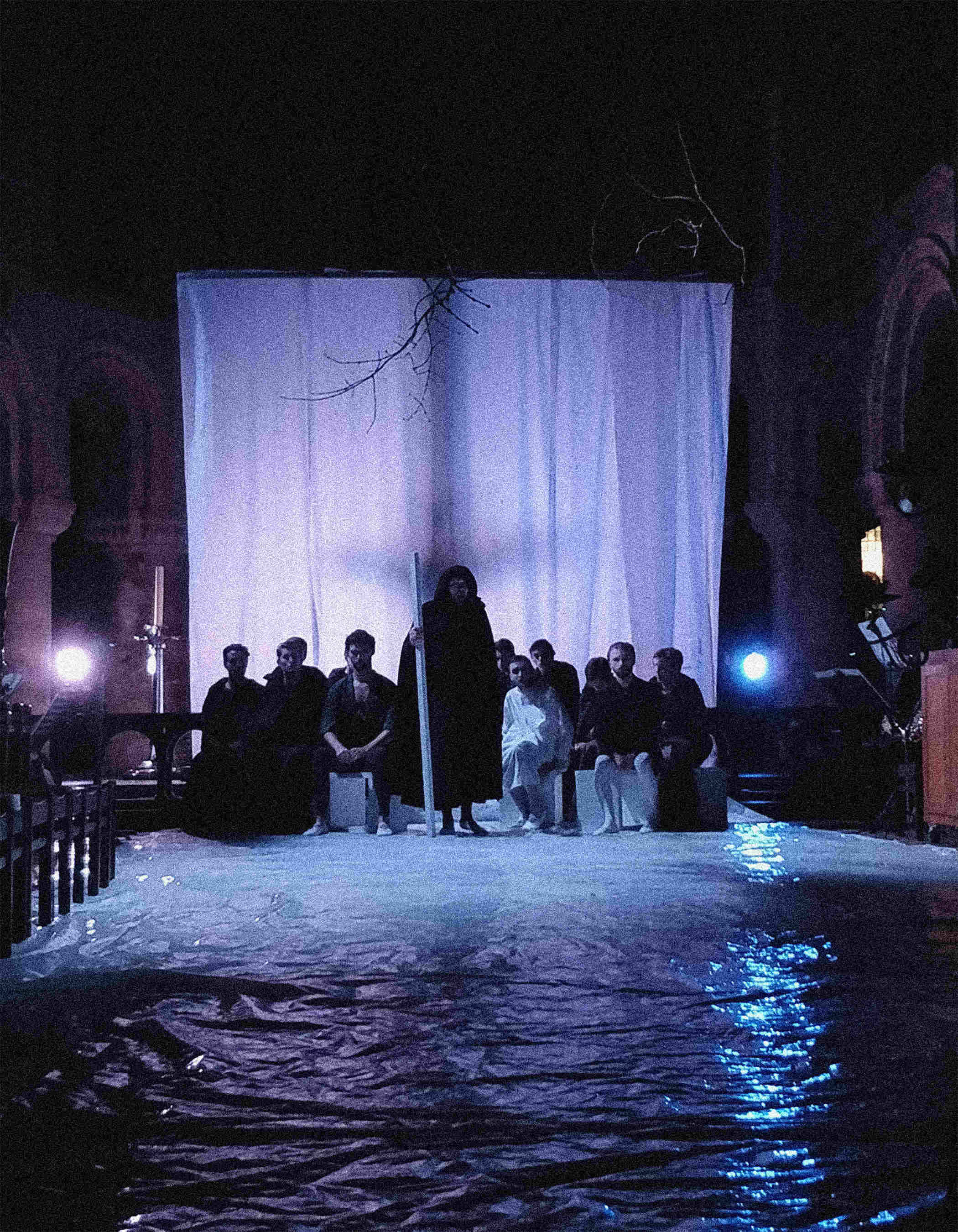 A silhouetted crucifix looms over the performers and a moonlit river